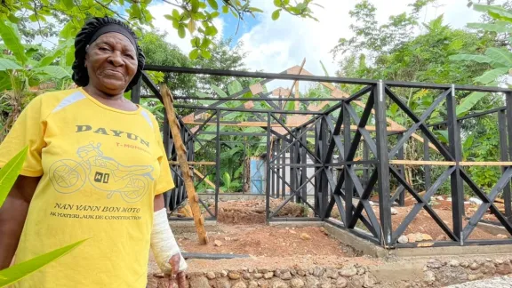 Woman wearing a yellow tshirt posing in front of a house under construction in Haiti
