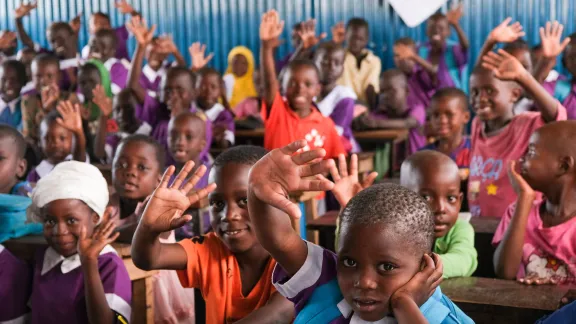 Kids in Kenya in a classroom raising hands