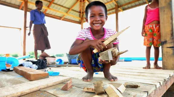 Young boy smiling carrying pieces of woods smiling at the camera in Myanmar 